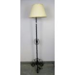 A vintage wrought iron standard lamp painted black, with scrolled and fleur de lis detail, on a