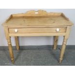 An antique stripped pine washstand, with shaped ¾ gallery, housing one long drawer with ceramic knob