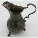 A silver cream jug with embossed decoration & trefoil feet. Indistinct London hallmarks, makers