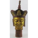 A large Chinese gilt and lacquer painted bronze Buddha head. Supported on a cylindrical wood plinth.