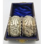 A pair of silver napkin rings heavily embossed with scrolls and foliate design, monogrammed,