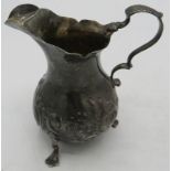A silver cream jug with embossed decoration & trefoil feet. Indistinct London hallmarks, makers
