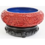A Chinese cinnabar lacquer bowl. With openwork carved wood stand. 7.5 in (19 cm) diameter. Condition