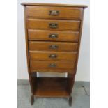 An Edwardian oak music cabinet, housing six long drawers with hinged fronts, above an open shelf, on