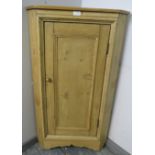 An antique stripped pine floor standing corner cupboard, the panelled door opening onto one fitted