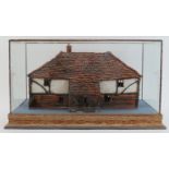 A painted terracotta model of a country cottage, 20th century. Housed within a glass display case.