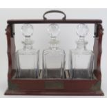 A three glass decanter tantalus set, 20th century. With brass mounts. 16 in (40.7 cm) length.