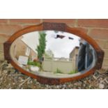 An Arts & Crafts bevelled oval wall mirror within an oak surround with relief carved scrolled