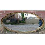 A reproduction oval wall mirror in a shaped and dished gilt surround. H54cm W111cm D4cm (approx).
