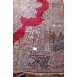 A mid 20th century Persian carpet with a large central floral motif on a red ground with deep 52cm