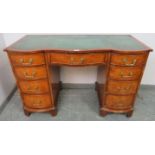 An antique style walnut serpentine front kneehole desk with inset green leather writing surface,