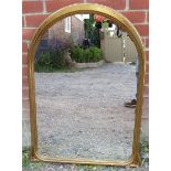 A reproduction arched overmantel mirror in a giltwood frame with carved foliate detail to corners.