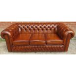 A vintage three-seater Chesterfield sofa upholstered in tobacco brown buttoned leather, raised on