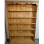 An antique pine tall bookcase, the shaped canopy above six open shelves, on a plinth base. H184cm