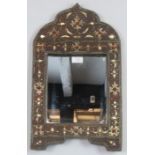 A vintage Eastern wall mirror within a shaped leather surround with applied brass and coral