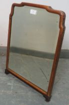 An early 20th century easel mirror, the bevelled glass plate within a shaped walnut surround, on