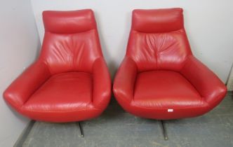 A pair of contemporary swivel lounge chairs, upholstered in red leather, on steel quatreform