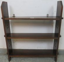 An Arts & Crafts oak wall hanging bookshelf, of three open shelves, having pierced trefoil detail to