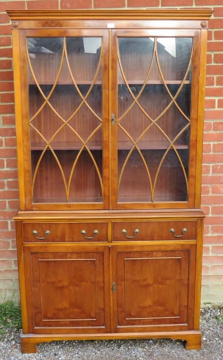 A reproduction yew wood tall glazed bookcase, having tracery doors opening onto two height-