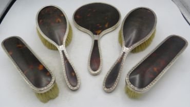 A five piece silver and tortoiseshell dressing table set comprising hand mirror, two hair brushes