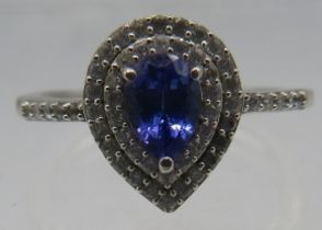 A silver tanzanite pear cut ring with surrounding rows of white stones & white stone shoulders.
