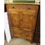 A reproduction oak side cabinet with carved upper drawer over twin panelled cupboard doors