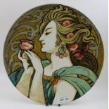 A French Art Nouveau earthenware charger, painted with a young woman in profile admiring a flower, s