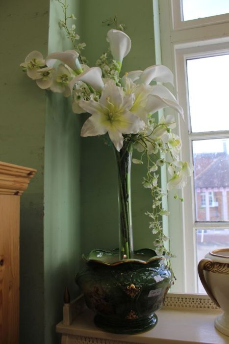 A green plant pot together with a tall glass vase containing artificial flowers