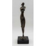 A late 20th century bronze cast female figure, in a standing, contemplative pose, raised on black pl