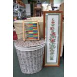 A glazed and framed poppy tapestry with a child's abacus and a woven wicker laundry basket.
