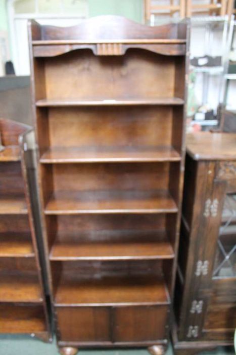 A slender oak finished set of shelves having lower cupboard on squashed bun feet