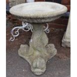 A small stone bird bath raised on ornate fish design support