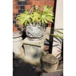 An ornate stone effect planter on non matching plinth with a small round planter and a small