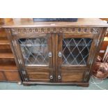 An oak finished side cupboard having carved freeze over twin diamond leaded doors