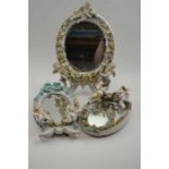 Three Continental porcelain framed mirrors, each with putti ad floral encrusted decoration, the larg