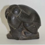 A 20th century Inuit soapstone carving, a squatting figure, with seal over shoulder, incised marks