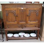A reproduction carved oak cupboard with arched doors over two drawers with pot shelf base