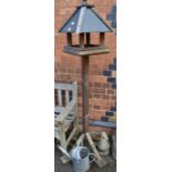 A slate roof house effect tall bird feeding table with a metal one gallon watering can