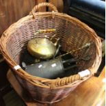 A wicker log basket containing a selection of brass and copper domestic items
