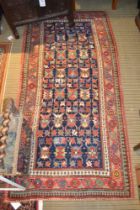 An antique Kazak rug, the blue ground with overall stylized designs, deeply bordered in red, 2.35m x