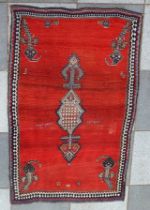 An old Persian Gabbeh rug, deep orange red ground, having central device with floral decoration