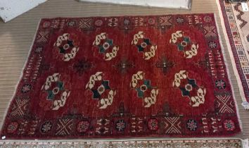 A red ground Turkoman rug, styled motifs in cream and blue, fringed 178cm x 127cm