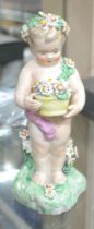 A porcelain figurine of a naked putti on a flower encrusted base, garlanded with flowers, and holdin