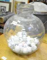 A clear glass carboy containing golf balls