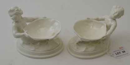 A pair of Royal Worcester bone china salts, modelled in the form of shells supported by Merboys, gre