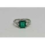 A hallmarked platinum emerald and diamond three stone ring, set with a central emerald-cut emerald