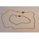 A string of pearls with purple stone clasp, approx. length 36cms and a string of pearls with