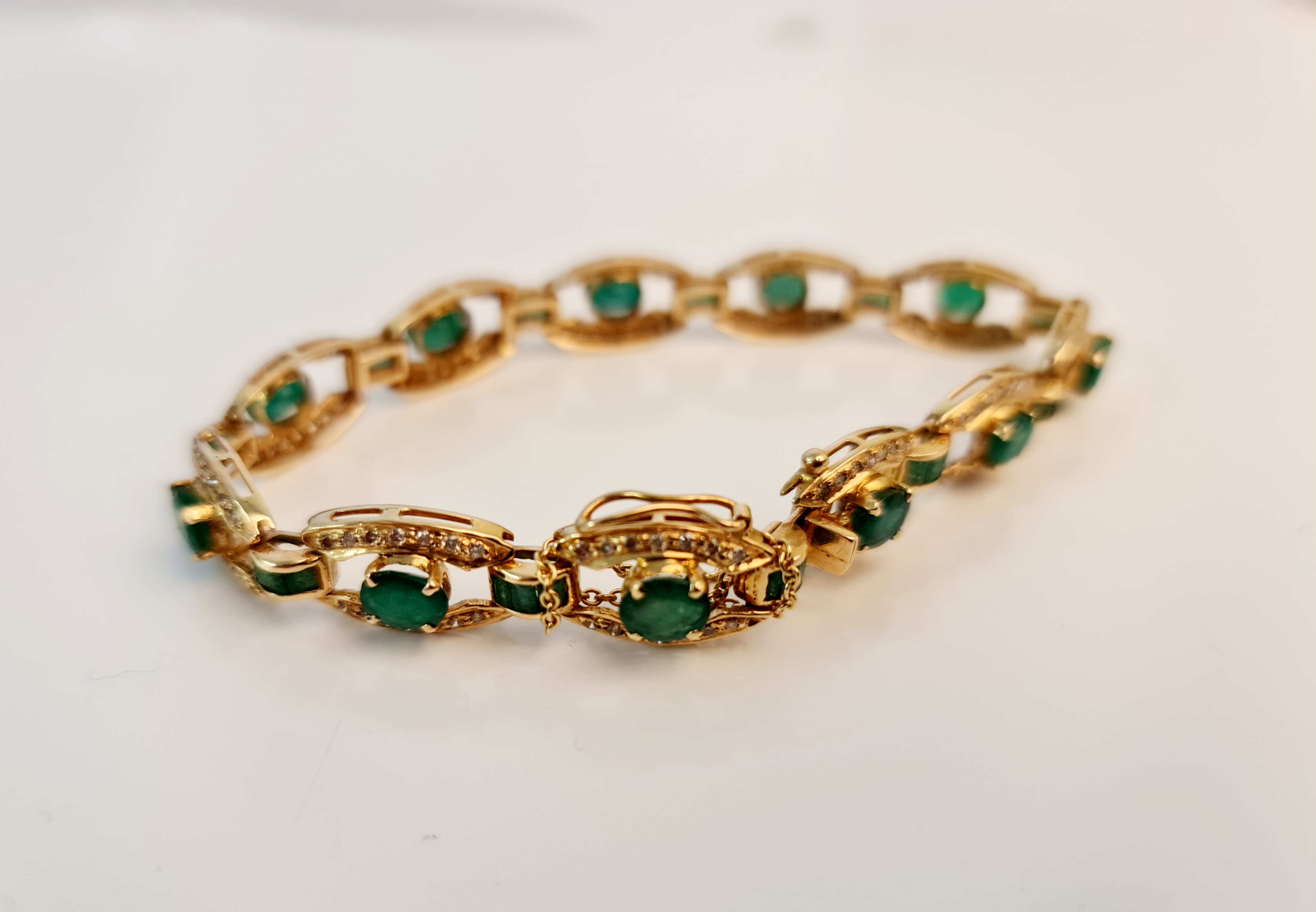 An emerald and diamond bracelet, each open metalwork oval design link set with a central oval cut