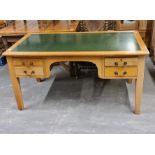 A golden oak four drawer desk with green top on square legs.