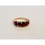 A hallmarked 9ct yellow gold boat shaped ring of five graduated garnets with patterned shoulders,